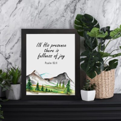 In His Presence There Is Fullness of Joy - Psalm 16:11 Bible Verse Wall Art with Mountains and Trees on White Background Wall Art displayed on the table in a black frame