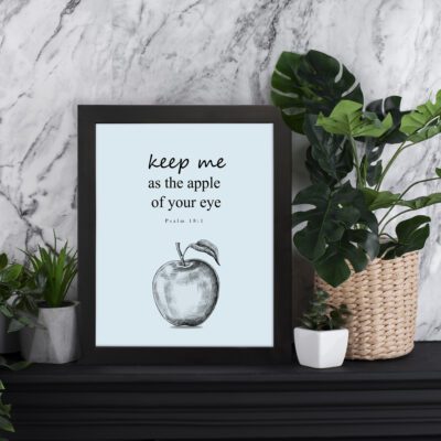 Keep Me As The Apple Of Your Eye Psalm 17:8 Bible Verse Wall Art with light blue background and a simple apple sketch. Wall Art displayed on the table in a black frame