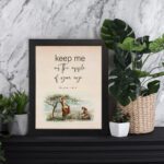 Psalm 17:8 wall art with a soft cursive font and a peaceful illustration of a person sitting under a tree. Wall art is displayed on the table in a black frame.