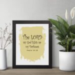 The Lord My God Lights Up My Darkness Psalm 18:28 Bible Verse Wall Art with decorative text on a light yellow paint stroke background. Wall Art displayed on the table in a black frame