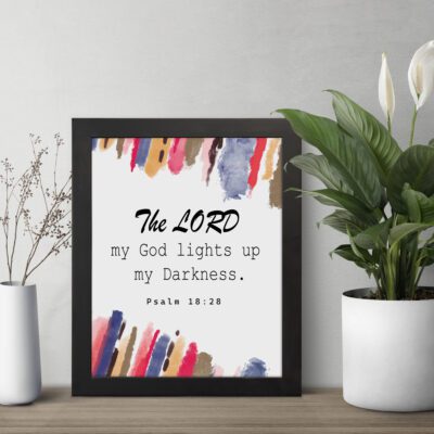 The Lord My God Lights Up My Darkness Psalm 18:28 Bible Verse Wall Art with black text and bold red, orange, blue, and yellow brush strokes on a white background. Wall Art displayed on the table in a black frame