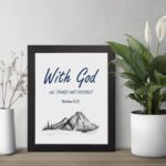 With God All Things Are Possible Matthew 19:26 Bible Verse Wall Art with dark blue text and mountain sketch on white background. Wall Art displayed on the table in a black frame