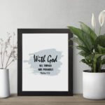 With God All Things Are Possible Matthew 19:26 Bible Verse Wall Art with black text and light blue brushstroke on white background. Wall Art displayed on the table in a black frame