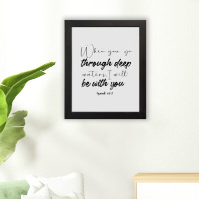 White wall art with black text in script and bold fonts quoting When you go through deep waters, I will be with you from Isaiah 43:2. hung on the floor in a black frame