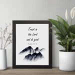 Infidu Trust In The Lord And Do Good Psalm 37:3 Bible Wall Art with black text and mountain illustration. Wall Art displayed on the table in a black frame