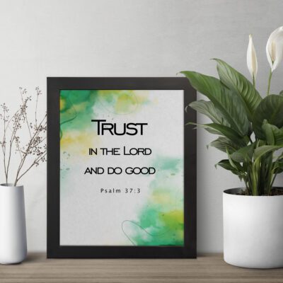 Trust in the Lord and Do Good Psalm 37:3 Bible Verse Wall Art with watercolor green and yellow background. Wall Art displayed on the wall in a black frame