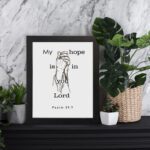 Infidu My Hope Is In You Lord Psalm 39:7 Bible Wall Art with a minimalist line drawing of figure in prayer and clean text Wall Art displayed on the table in a black frame