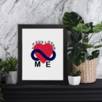 Infidu Jesus Loves Me Bible Wall Art with red heart and blue infinity symbol, with the text JESUS LOVES ME around the image Wall Art displayed on the table in black frame