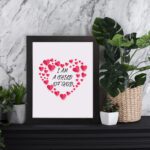 Infidu I Am A Child Of God Bible Wall Art with pink hearts and mixed cursive and print text on a light pink background Wall Art displayed on the wall in a black frame