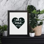 Infidu I Am A Child Of God Bible Wall Art with a dark green heart and white text on a white background Wall Art displayed on the table in a black frame