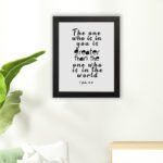 White wall art with black text reading The one who is in you is greater than the one who is in the world 1 John 4:4. hung on the floor in a black frame