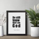 Be Still and Know That I Am God Psalm 46:10 Bible Verse Wall Art with bold black text on a white background. Wall Art displayed on the table in a black frame