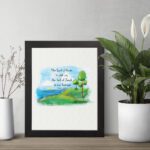 Psalm 46:7 Bible verse wall art with serene watercolor landscape of trees, hills, and water, featuring the verse in black text. displayed on the table in a black frame