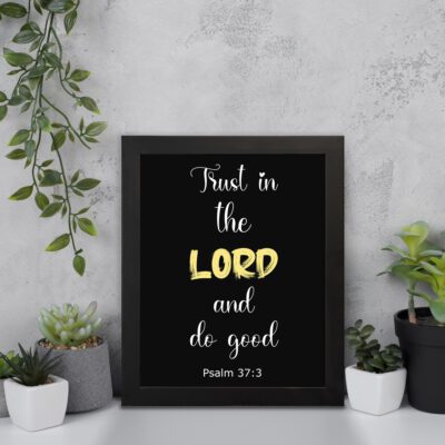 Psalm 37:3 Bible verse wall art with a black background, Lord highlighted in yellow. Christian home decor by Infidu. Wall Art displayed on the wall in a black frame