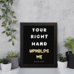 Infidu Your Right Hand Upholds Me Psalm 63:8 Bible Wall Art with a black background, yellow, and white font, and white frame displayed on the wall