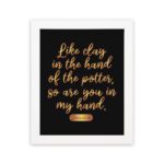 Infidu wall art with the text Like clay in the hand of the potter, so are you in my hand in golden letters on a black background. hung on the wall in a white frame