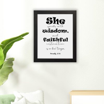 Proverbs 31:26 Bible wall art featuring bold and simple fonts on a white background, framed in black, highlighting the message of wisdom. hung on the floor in a black frame