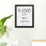 The Lord My God Lights Up My Darkness Psalm 18:28 white text on a black background with a black frame Christian wall art. hung on the floor in a black frame