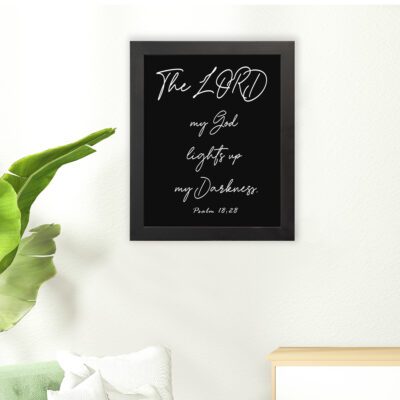 The Lord My God Lights Up My Darkness Psalm 18:28 white handwritten text on black background Christian wall art hung on the floor in a black frame