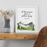 In His Presence There Is Fullness of Joy - Psalm 16:11 Bible Verse Wall Art with Mountains and Trees on White Background Wall Art displayed on the table in a white frame