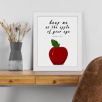 Keep Me As The Apple Of Your Eye" Psalm 17:8 Bible Wall Art featuring a red apple and white background. Perfect Christian home decor. Wall Art displayed on the table in white frame