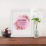 The Lord My God Lights Up My Darkness Psalm 18:28 Bible Verse Wall Art with black text on a soft pink watercolor background and delicate floral accents. Wall Art displayed on the wall in a white frame