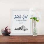 With God All Things Are Possible Matthew 19:26 Bible Verse Wall Art with dark blue text and mountain sketch on white background. Wall Art displayed on the table in a white frame