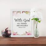 With God All Things Are Possible Matthew 19:26 Bible Verse Wall Art with black text and floral accents in pink and green on a white background. Wall Art displayed on the table in a white frame