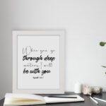 White wall art with black text in script and bold fonts quoting When you go through deep waters, I will be with you from Isaiah 43:2. displayed on the table in a white frame