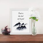 Infidu Trust In The Lord And Do Good Psalm 37:3 Bible Wall Art with black text and mountain illustration. Wall Art displayed on the table in a white frame