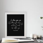 Black wall art with white text and small flower designs quoting When you go through deep waters I will be with you from Isaiah 43:2. displayed on the table in a white frame