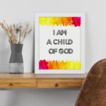 Infidu I Am A Child Of God Bible Wall Art with colorful watercolor borders and black block text on a white background Wall Art displayed on the table in a white frame