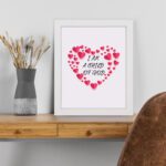 Infidu I Am A Child Of God Bible Wall Art with pink hearts and mixed cursive and print text on a light pink background Wall Art displayed on the table in a white frame