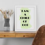 Infidu I Am A Child Of God Bible Wall Art with light green shape and black text on a white background Wall Art displayed on the table in a white frame