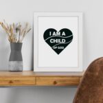 Infidu I Am A Child Of God Bible Wall Art with a dark green heart and white text on a white background Wall Art displayed on the table in a white frame