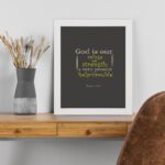 Psalm 46:1 Bible Wall Art with muted text on a dark gray background, featuring varying fonts and sizes. Wall Art displayed on the table in a white frame