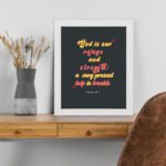 Psalm 46:1 Bible Wall Art with bold, colorful text on a deep black background. Wall Art displayed on the table in a white frame