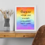 Psalm 46:1 Bible Wall Art with black vertical text on a vibrant rainbow gradient background. Wall Art displayed on the table in a white frame