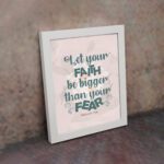 Christian wall art with greenish-blue 'Faith' and 'Fear' text on a light peach floral background. Wall Art displayed on the wall in a white frame