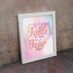 Let Your Faith Be Bigger Than Your Fear Christian wall art with pink and red script font and pastel watercolor background. Wall Art displayed on the wall in a white frame