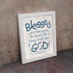 Infidu Matthew 5:8 Christian wall art with blue text on a white background, featuring a subtle pastel floral design and stylized GOD. Wall Art displayed on the wall in a white frame