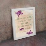 Infidu Jeremiah 18:6 Christian wall art with green and purple text on a light beige background, decorated with purple flowers in the corners. Wall Art displayed on the wall in white frame