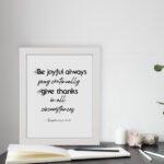 Infidu wall art with the text Be joyful always, pray continually, give thanks in all circumstances from 1 Thessalonians 5:16-18. displayed on the table in a white frame