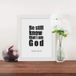 Be Still and Know That I Am God Psalm 46:10 Bible Verse Wall Art with bold black text on a white background. Wall Art displayed on the table in a white frame