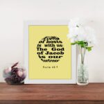 Infidu The Lord Of Hosts Is With Us Psalm 46:7 Bible Verse Wall Art on light yellow background. displayed on the table in a white frame