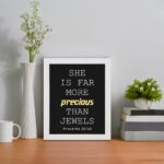 Proverbs 31:10 wall art with precious gold on a black background, featuring minimalist design and modern font. displayed on the table in a white frame