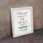 Zechariah 4:6 Christian Wall Art with minimalist design, dark brown text, and teal LORD on a light white floral background. Wall Art displayed on the wall in a white frame