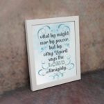 Zechariah 4:6 Bible verse wall art with light blue and white text, decorative flourishes, and a light blue gradient background. Inspiring Christian home decor. Wall Art on the kept wall in a white frame