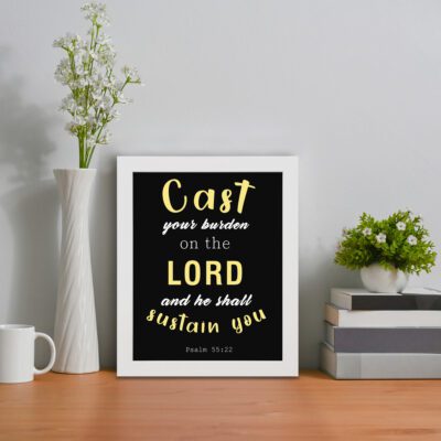 Christian wall art with a black background, yellow and white font, featuring Psalm 55:22 and Zechariah 4:6 Bible verses in a white frame displayed on the table