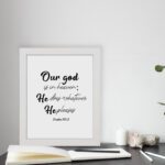 Bible verse wall art with Psalm 115:3 in black text on a white background. Modern design with cursive and standard fonts. displayed on the table in a white frame